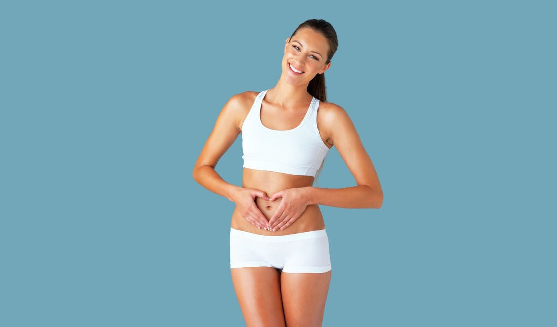 Smiling woman in white activewear making a heart shape over stomach, promoting digestive health