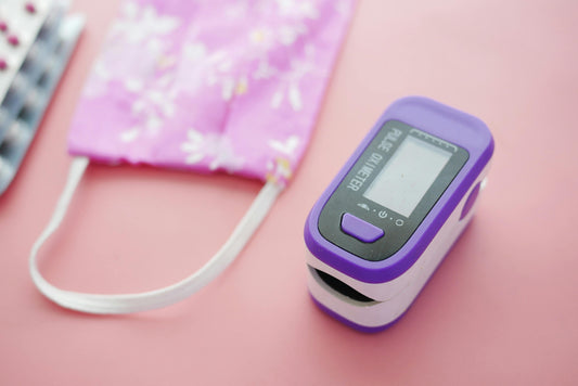 Purple pulse oximeter, face mask, and blister pack on pink medical supplies background