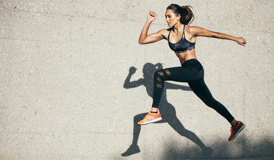 Athletic woman in sportswear jumping outdoors against a concrete wall, fitness training concept