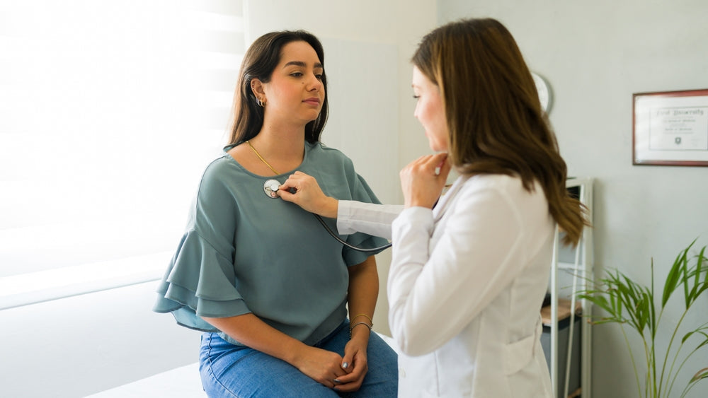 Doctor using stethoscope for medical checkup on woman in UK GP clinic exam room