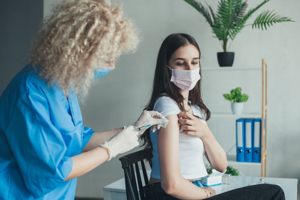 Healthcare worker giving vaccine injection to young woman wearing mask in medical clinic