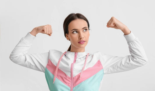 Woman in pastel sporty jacket flexing arms, symbolizing strength and wellness
