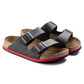 Black two-strap sandals with buckles, cork footbed, and red-accented sole on white background