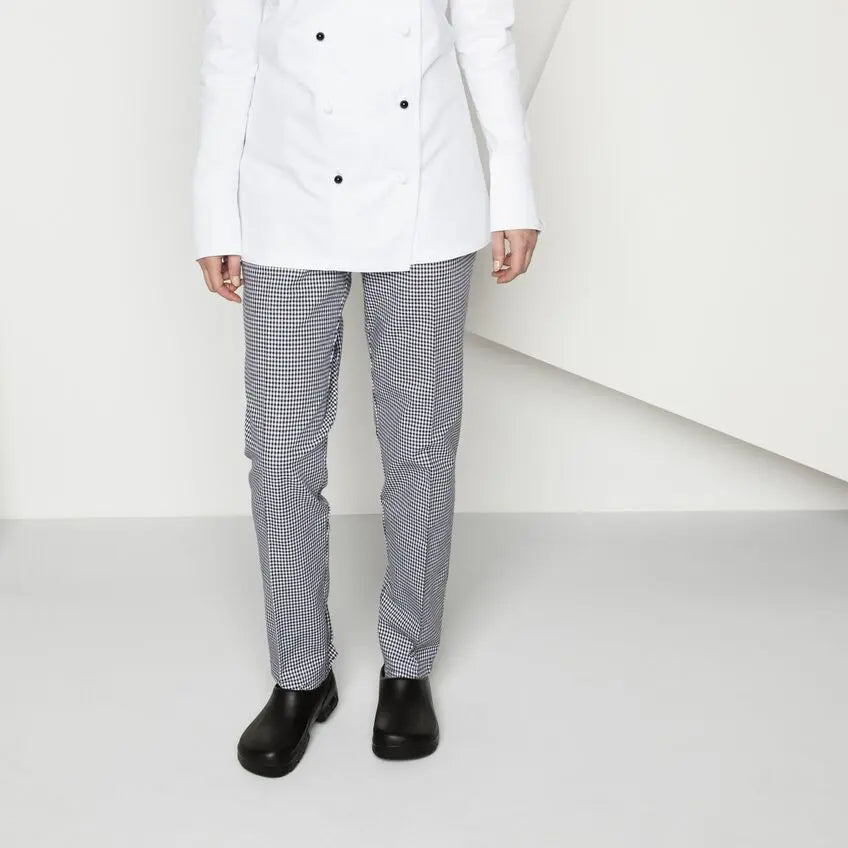 Person wearing a white chef jacket, checkered chef trousers, and black work shoes