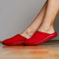 Person wearing bright red closed-toe slippers on a wooden floor, comfortable indoor footwear.