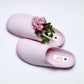 Pair of pink medical slippers with green cross tag and fresh pink roses on white background