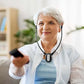 Older woman using amplified wireless TV headphones and holding a remote on a sofa