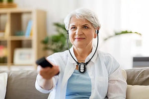 Older woman using amplified wireless TV headphones and holding a remote on a sofa