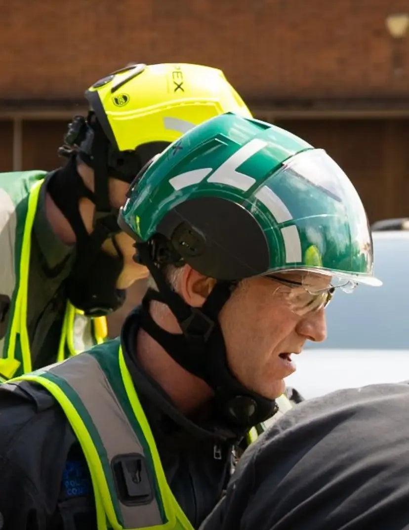 Emergency personnel wearing protective helmets and hi-vis vests in an outdoor medical response